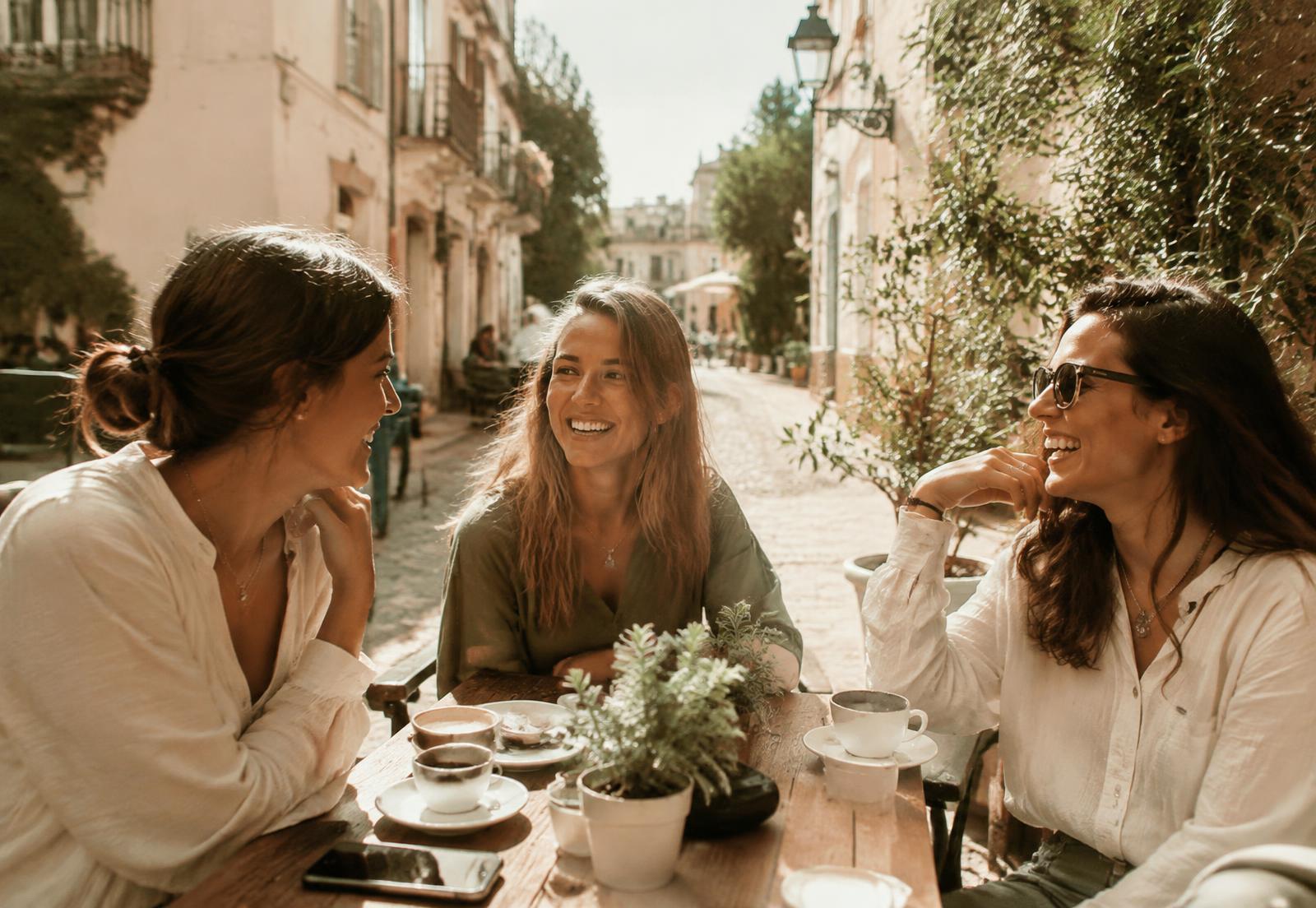 Friends laughing over coffee at a sunny street café